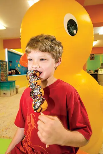 Kid sitting by the duck enjoying his donutz on a stick